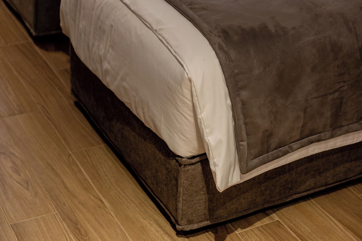 Two beds with brown headboards and white bedding, a wooden floor, and a curtain in the background.