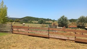 Cerca de madeira em ambiente rural, com fardos de feno e equipamento agrícola ao fundo.