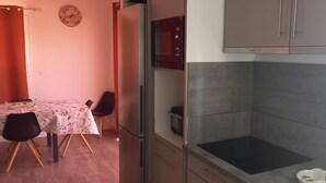 Uma cozinha com fogão embutido, micro-ondas e armários. Há uma mesa de jantar com cadeiras e um relógio na parede.