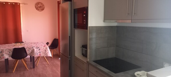 Una cocina con estufa integrada, microondas y armarios. Hay una mesa de comedor con sillas y un reloj en la pared.