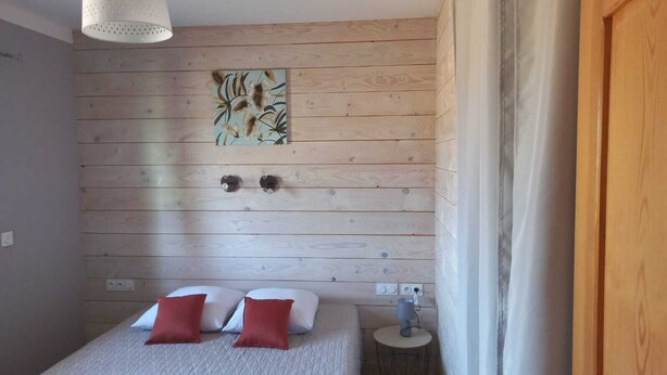 Quarto com parede de madeira, cama com duas almofadas, luminária de parede e uma tomada.