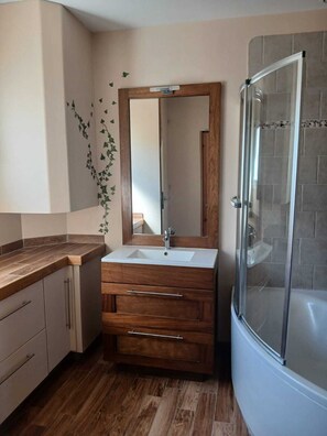 A bathroom with a wooden vanity, a mirror, a sink, and a glass-enclosed shower. - Vacation Home (Montmeyan)