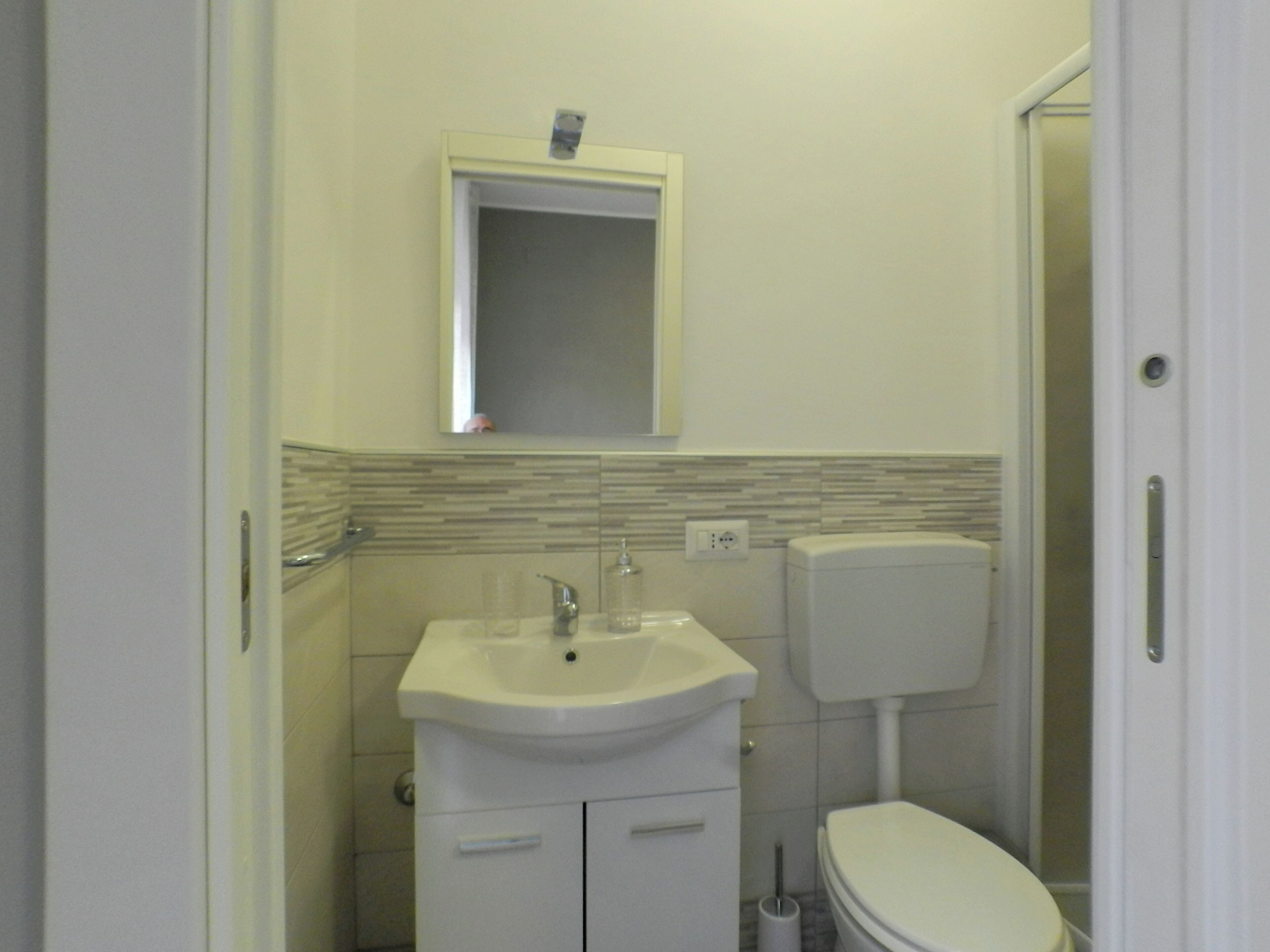 Een kleine badkamer met een wit wastafel, spiegel en toilet.