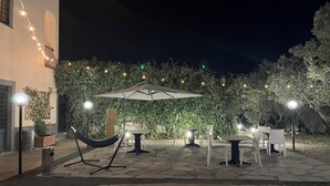 Un patio al aire libre con luces colgantes, una hamaca, mesas, sillas y un paraguas grande.