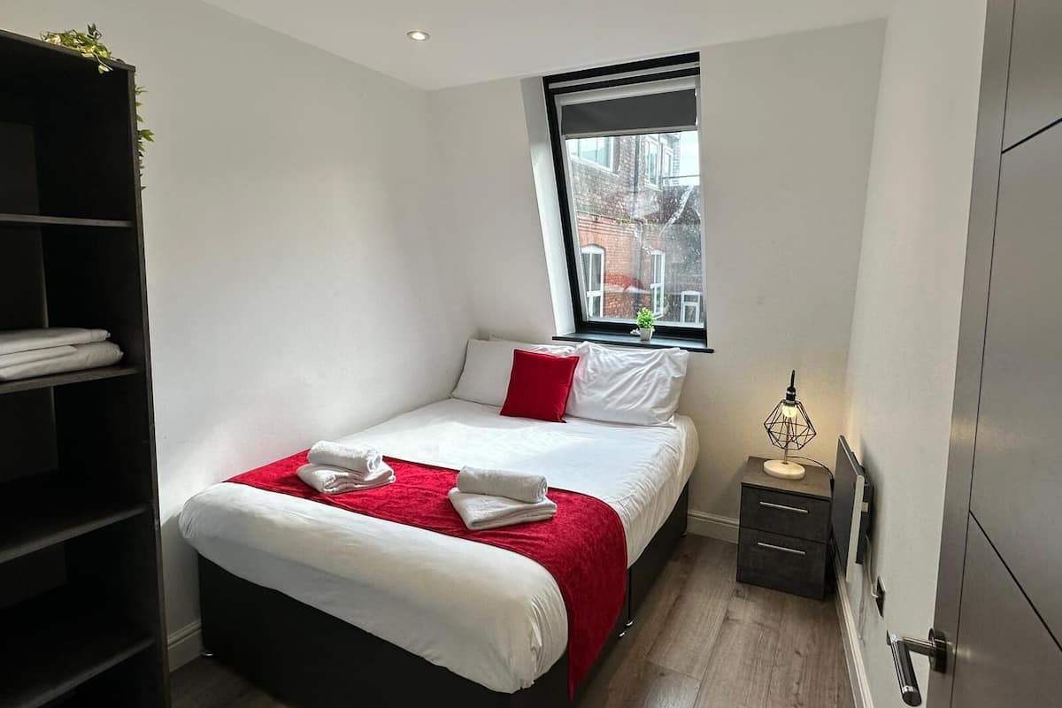 Une chambre d’hôtel moderne, équipée d’un lit, d’une table de chevet, d’une armoire et d’une fenêtre donnant sur des immeubles.