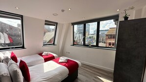 Una habitación de hotel moderna con dos camas, ventanas amplias y vistas a la ciudad.