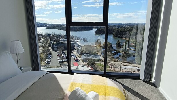 Ein Hotelzimmer mit großem Fenster und Blick auf einen See sowie umliegende Gebäude.