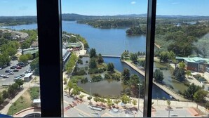 Blick aus einem Fenster in einem Hochhaus auf einen Fluss, eine Brücke und einen Parkplatz mit Bäumen und Gebäuden.
