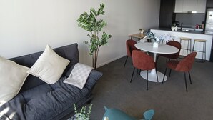 Ein modernes Wohnzimmer mit einem grauen Sofa, einem Esstisch mit roten Stühlen und einer Küche im Hintergrund.