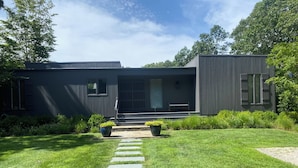 Una casa moderna con un sendero pavimentado que conduce a la puerta principal, rodeada de césped cuidado y plantas en macetas.