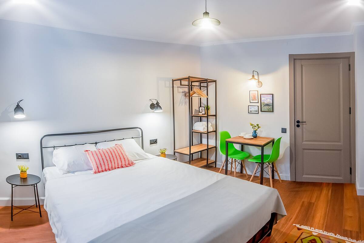 A neatly arranged bedroom with a bed, bedside tables, a desk with chairs, and a wardrobe.