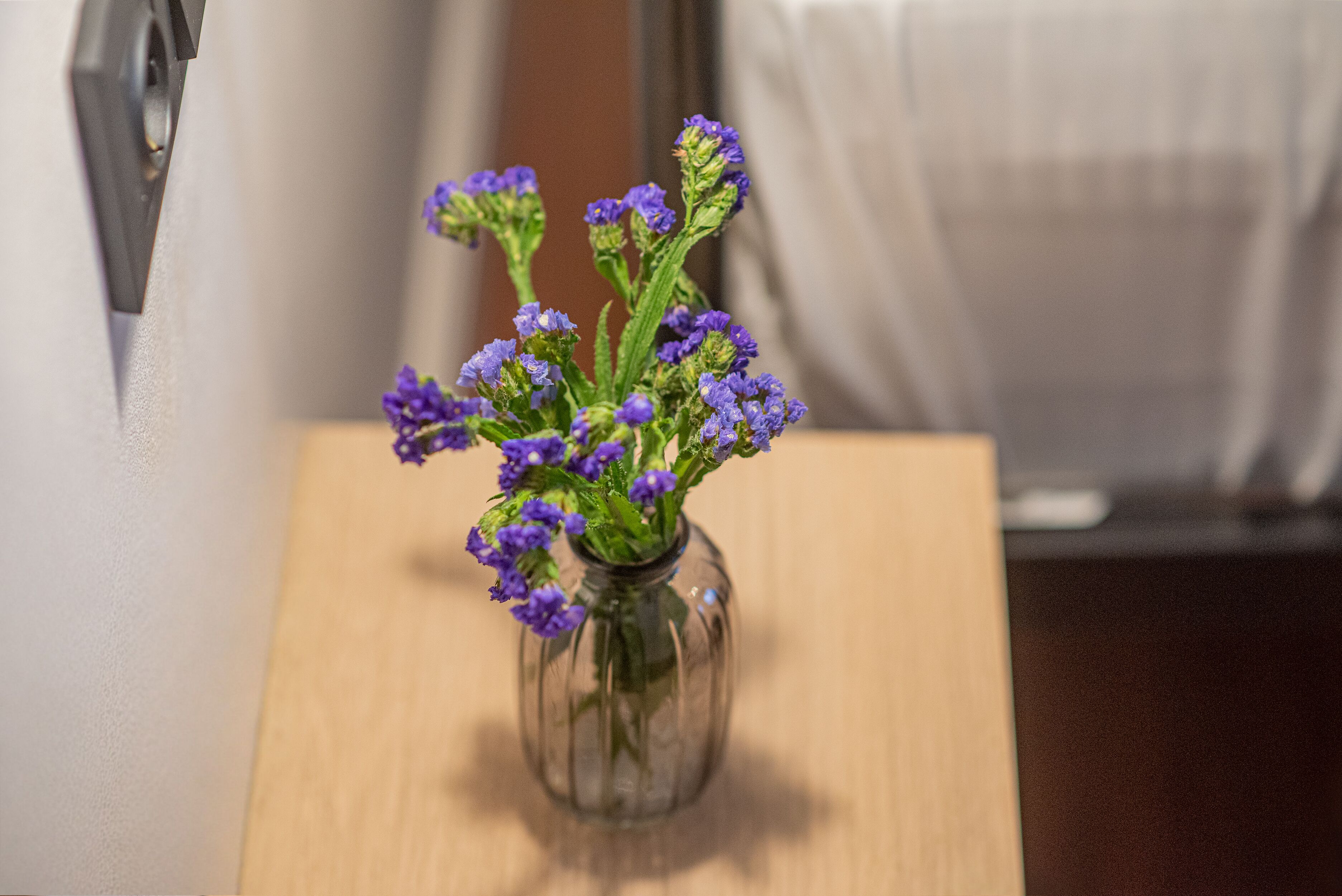 A clear view of a small glass vase with purple flowers on a wooden surface.