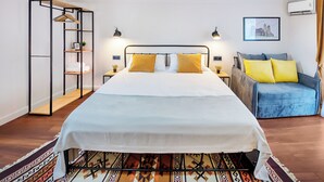 Un dormitorio con cama, sofá azul, estantería y aire acondicionado instalado en la pared.