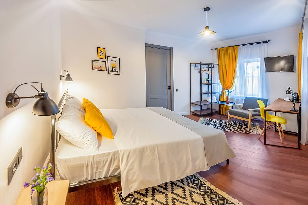 A well-lit hotel room with a bed, bedside lamp, and a desk with a chair.