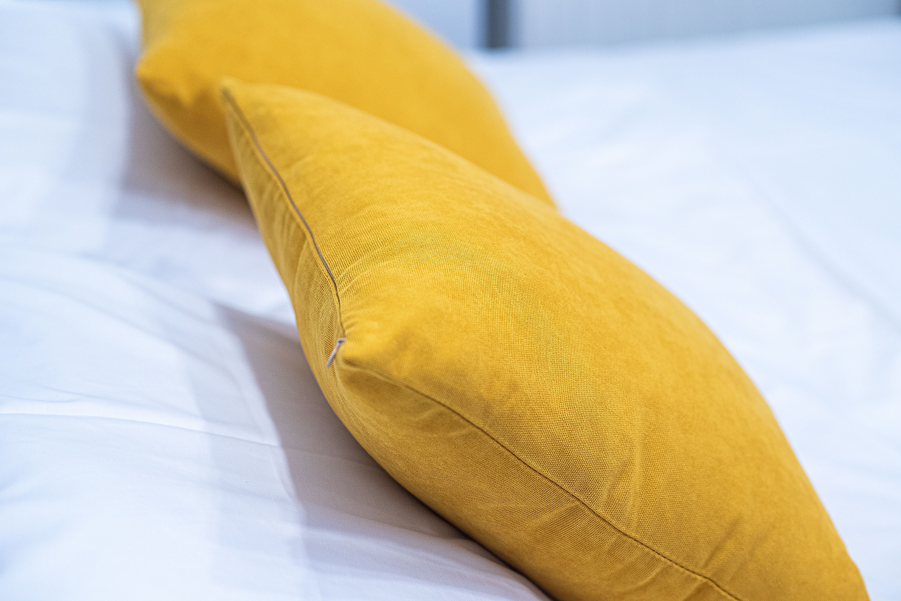 A bed with white sheets and two yellow pillows.