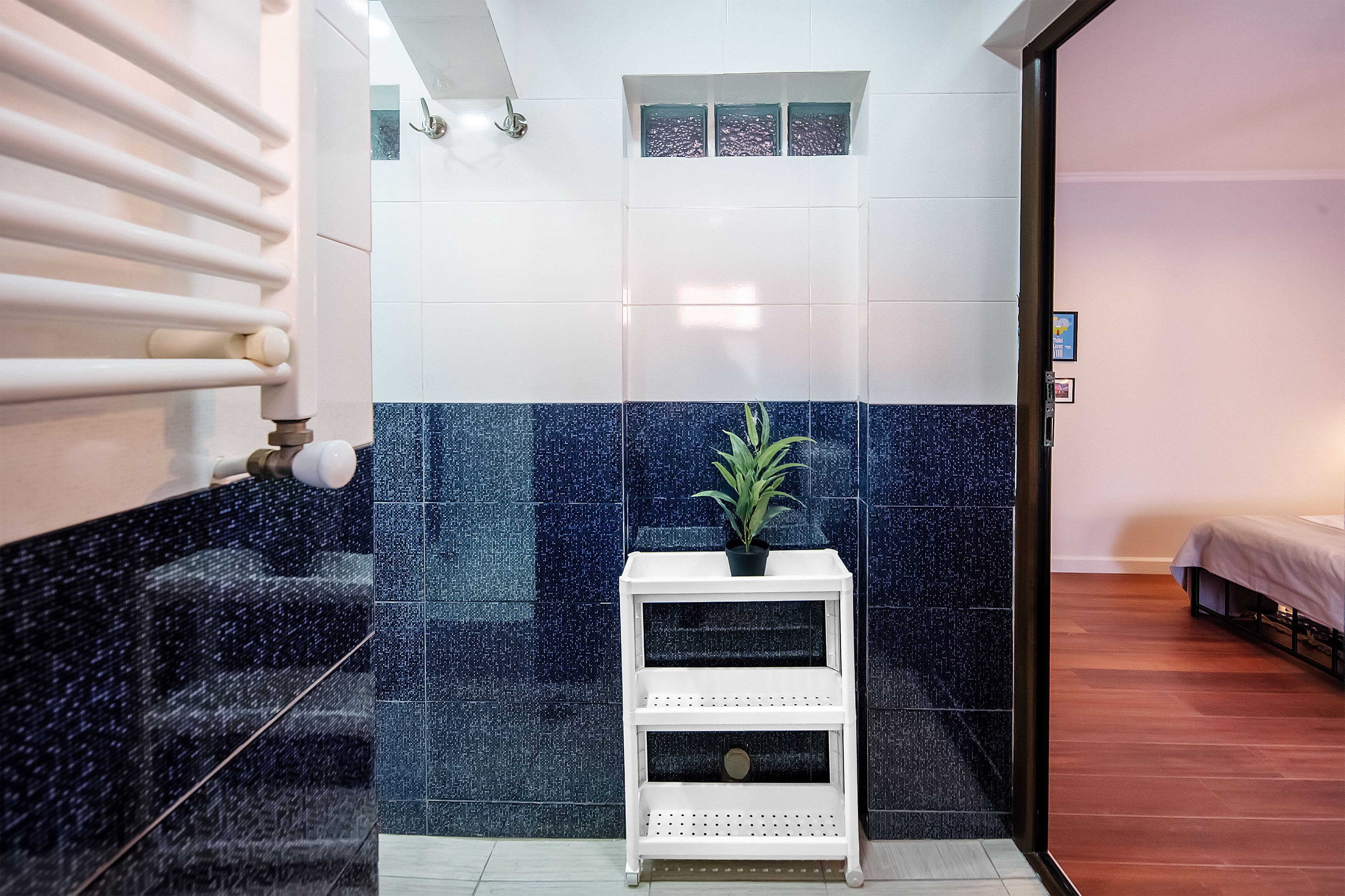 A bathroom with a white vanity, a shower area, and a bed in the adjacent room.