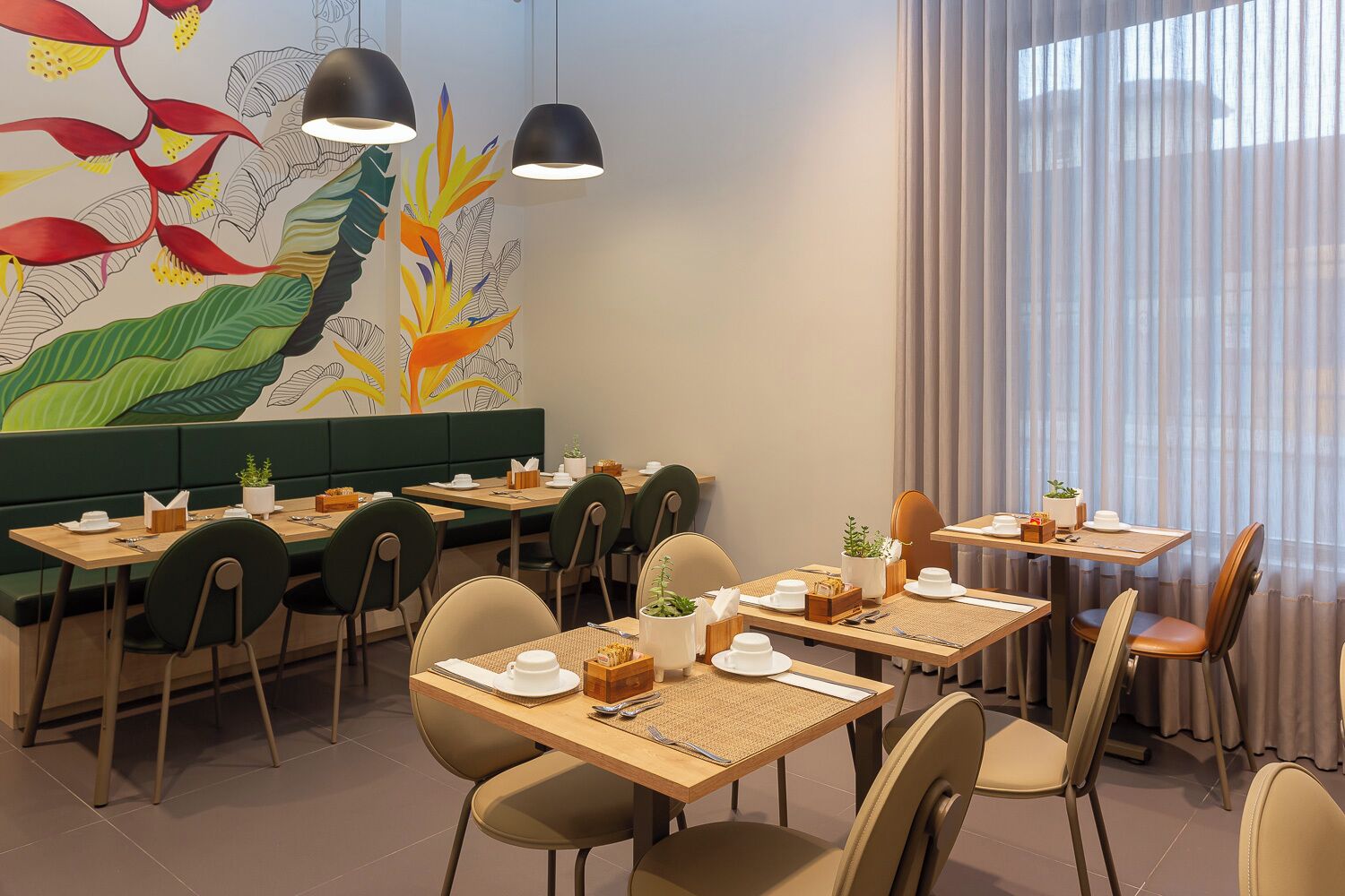 Un restaurante con varias mesas y sillas, un mural con motivos vegetales e iluminación colgante.