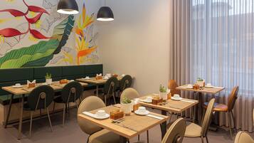Un restaurante con varias mesas y sillas, un mural con motivos vegetales e iluminación colgante.