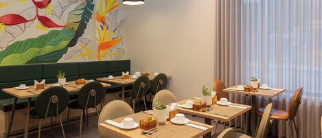 A restaurant with multiple tables and chairs, a mural with plant designs, and pendant lighting.