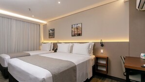Une chambre d’hôtel avec deux lits, un bureau et une chaise. Il y a deux lampes fixées au mur et un téléphone sur le bureau.