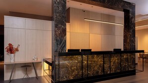 Un comptoir d’accueil avec un revêtement en marbre, un luminaire moderne et un espace détente agrémenté d’un vase de fleurs.