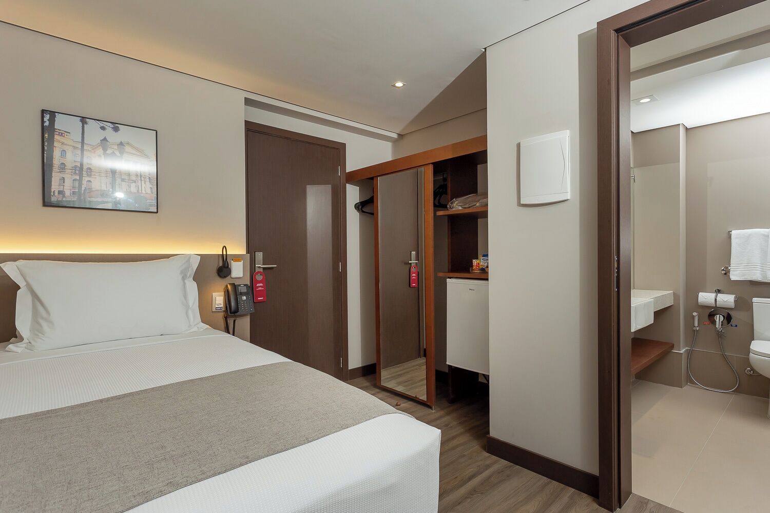 Habitación de hotel con cama, escritorio, teléfono, minibar y baño con inodoro y lavabo.