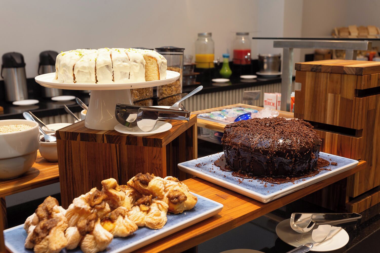 A buffet setup with a white cake, a chocolate cake, and assorted pastries on wooden serving boards.
