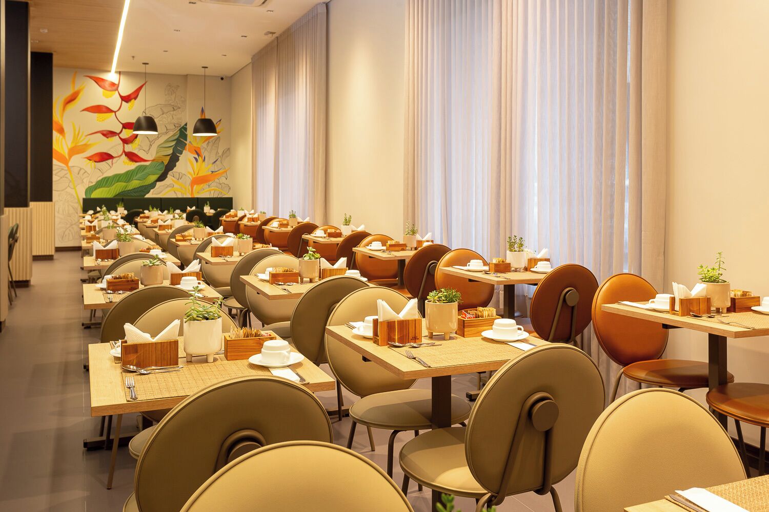 Un restaurante con varias mesas y sillas, cada conjunto con un mantel individual, un porta servilletas y una pequeña planta en maceta.