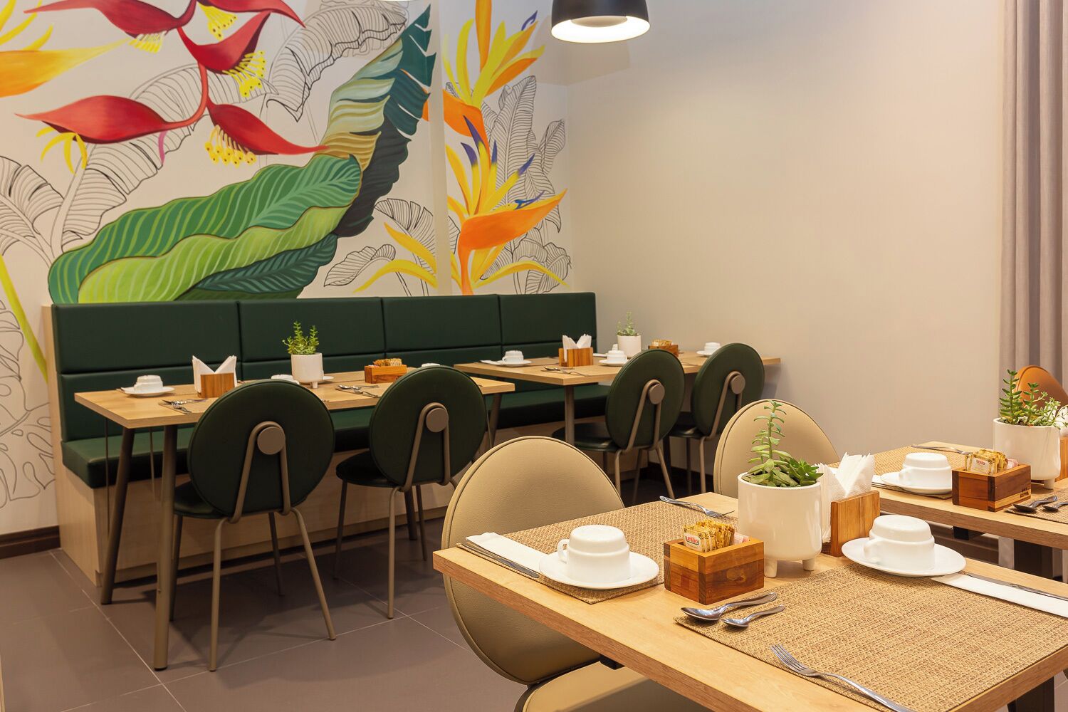 A restaurant with green booths and tables, white plates, and a mural of tropical plants on the wall.