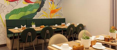 A restaurant with green booths and tables, white plates, and a mural of tropical plants on the wall.