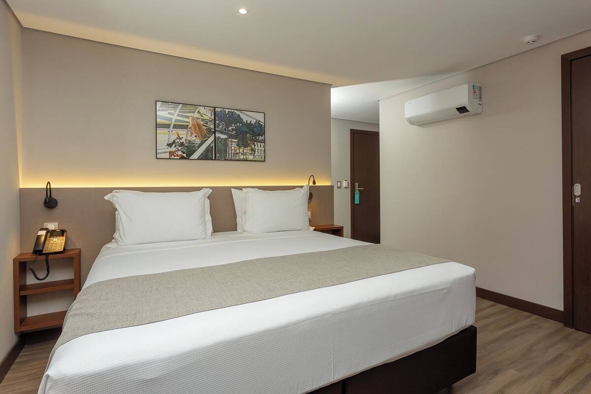 Une chambre d’hôtel moderne avec un grand lit, un téléphone sur la table de chevet et un climatiseur fixé au mur.