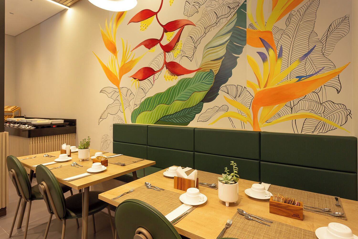 Un restaurante con mesas de madera, cabinas tapizadas de verde y un mural de plantas tropicales en la pared.