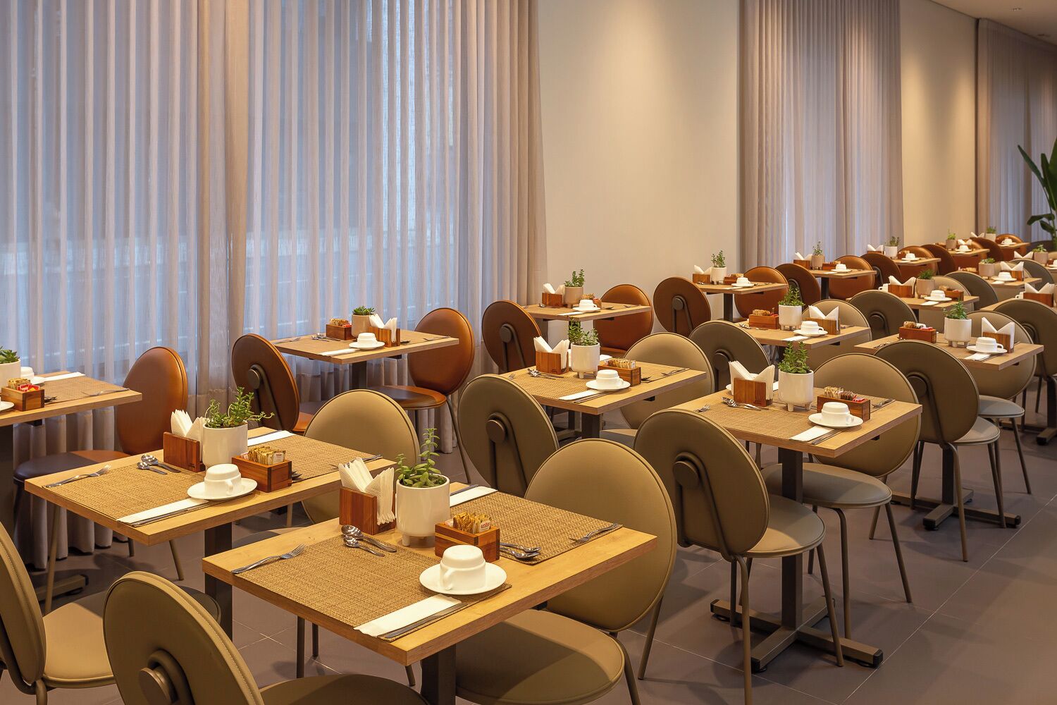 Ein Hotel-Speisesaal mit mehreren Tischen und Stühlen, jeweils gedeckt mit Besteck, Tellern und Servietten.