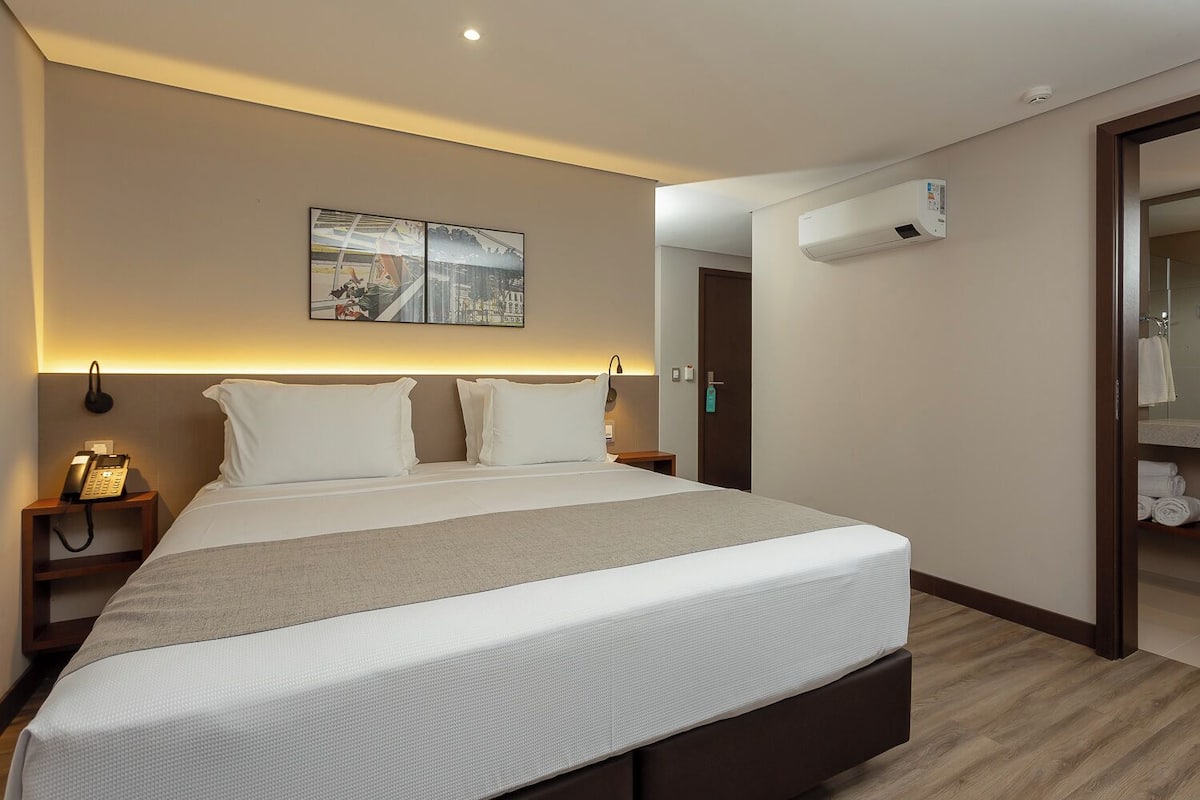 Une chambre d’hôtel moderne dotée d’un grand lit, de lampes de chevet, d’un téléphone, d’un appareil de climatisation et offrant une vue sur la salle de bain.