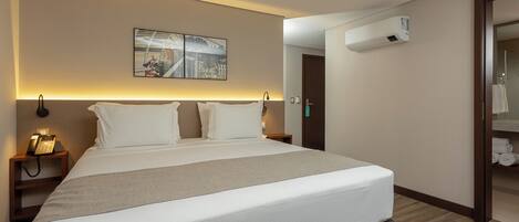 Una habitación de hotel moderna con una cama grande, lámparas de noche, un teléfono, un equipo de aire acondicionado y vistas al baño.