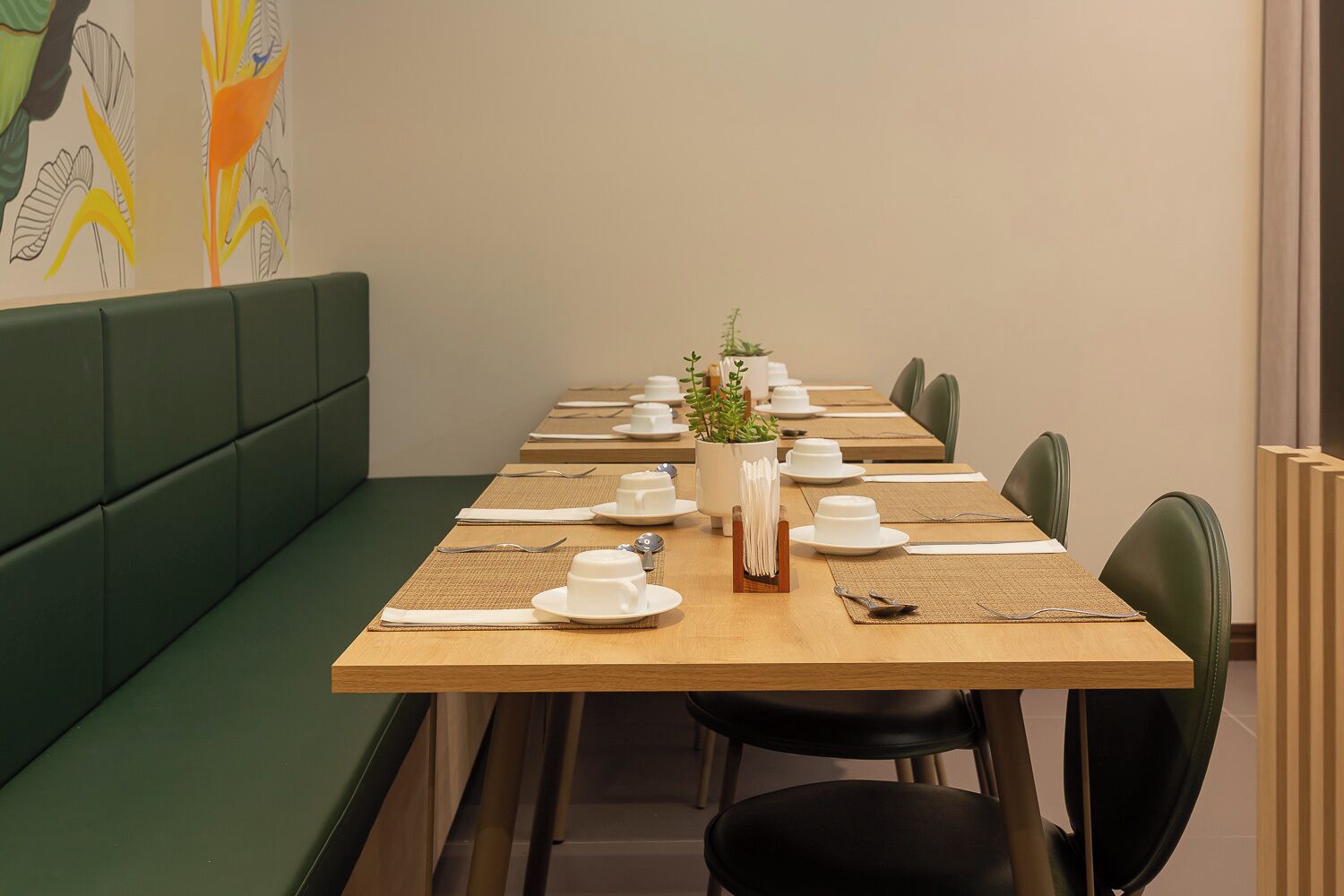 A dining area with a long wooden table set for a meal, surrounded by green upholstered seating.