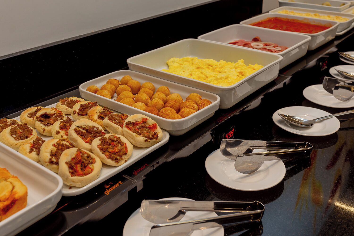 A buffet with various food options including meat-filled buns, scrambled eggs, and other dishes.