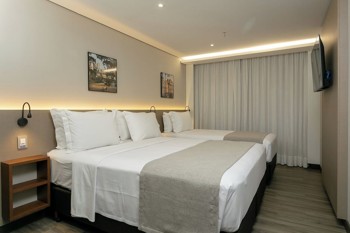 Une chambre d’hôtel avec un grand lit, des tables de chevet, un téléviseur à écran plat et deux œuvres d’art accrochées au mur.