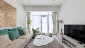 A modern living room with a sofa, a coffee table, a TV, and a large window with curtains.