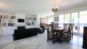 A spacious living room with a black sofa, a dining table with chairs, and a fireplace. Shelves with books and decorative items line the walls. - Tess Villa Becerra in Alhaurin de la Torre (Alhaurin de la Torre)