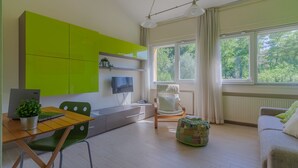 A modern living room with a dining area, a green sofa, a wooden table, and a TV.