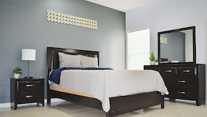 A modern bedroom with a bed, nightstands, a dresser, a mirror, and a decorative wall piece. - Elegant Apartment 10 min to Mercedes Outlets (Weslaco)