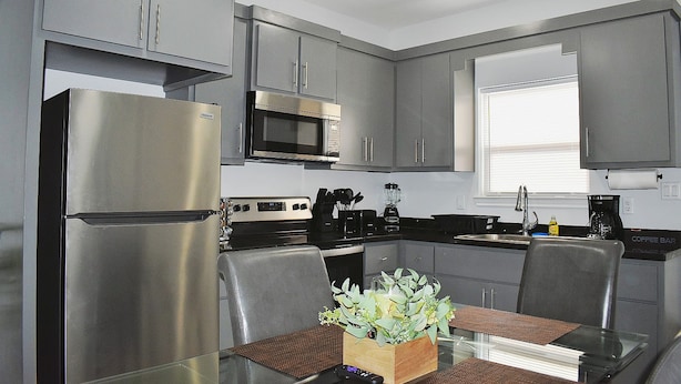A modern kitchen with grey cabinets, stainless steel appliances, and a dining area with a glass table and chairs. - Elegant Apartment 10 min to Mercedes Outlets (Weslaco)