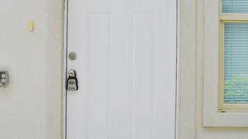 A white door with a keypad lock, a doormat with "hello" written on it, and a small window with blinds to the right.
