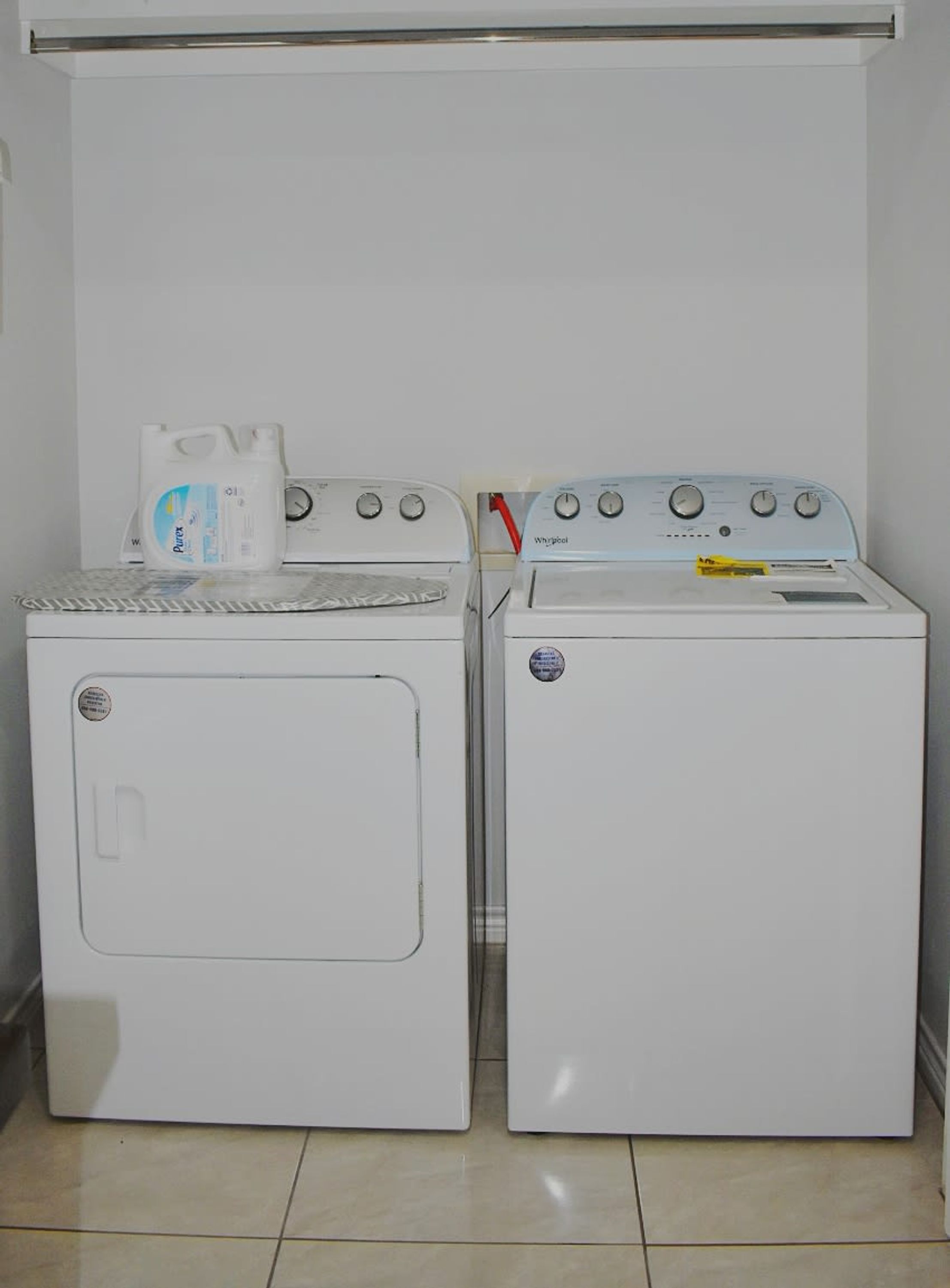 Deux machines à laver blanches à chargement frontal sont placées côte à côte dans une buanderie dont le sol est carrelé.
