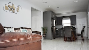 A modern living room with a brown leather sofa, a dining area with a table and chairs, and a kitchen with dark cabinets and a refrigerator. - Elegant Apartment 10 min to Mercedes Outlets (Weslaco)