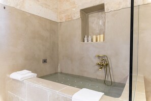 Ein modernes Badezimmer mit einer gläsernen Duschkabine, einer integrierten Ablagefläche mit Toilettenartikeln und ordentlich gefalteten Handtüchern.