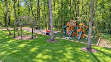 Un terrain de jeux avec des toboggans et une structure d’escalade, le tout entouré d’arbres.
