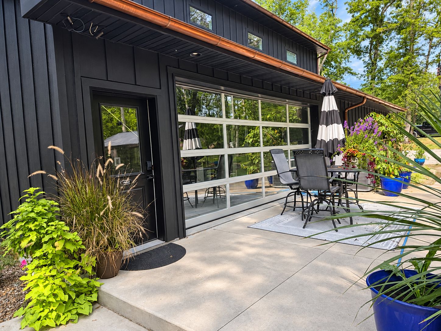 Une maison moderne dotée d’un portail de garage, d’un espace extérieur aménagé pour se détendre et de plantes en pot.