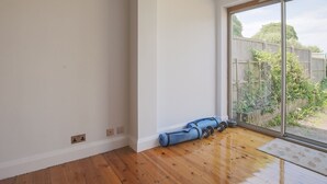 Ein geräumiges Zimmer mit Holzboden, einem großen Schiebeglastür zum Garten und Sportgeräten in der Nähe der Tür.